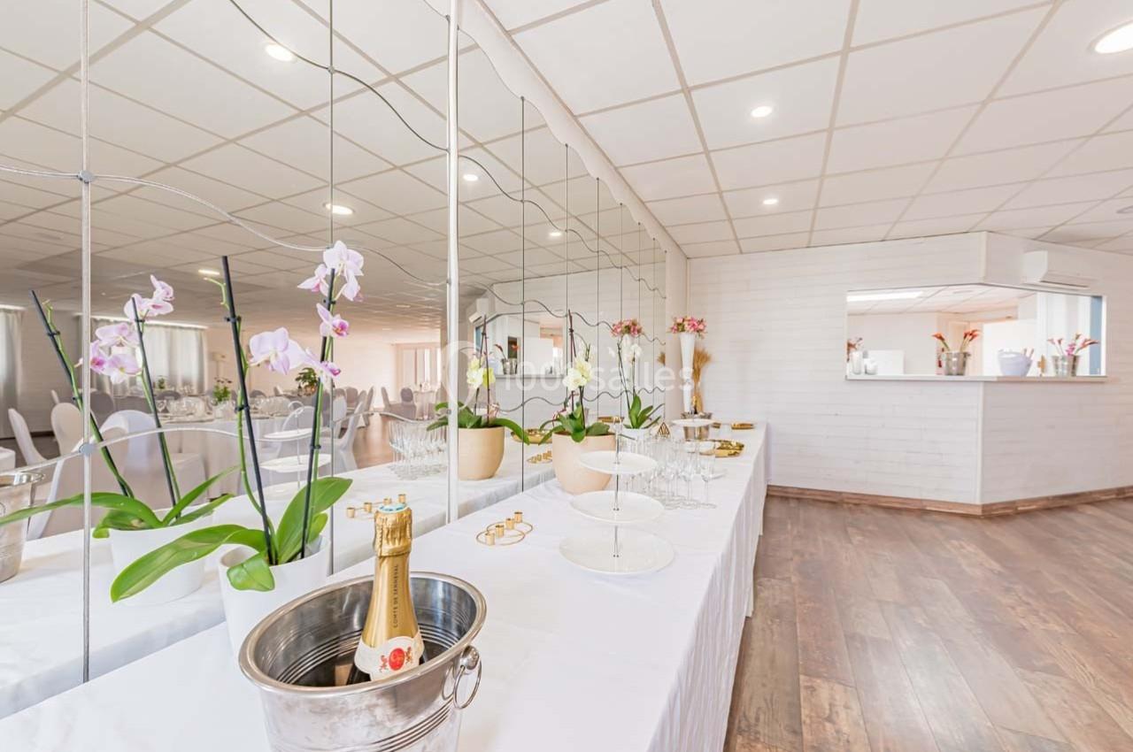 Table dressée avec des orchidées, des verres, une bouteille de champagne dans un seau et un décor lumineux en arrière-plan.