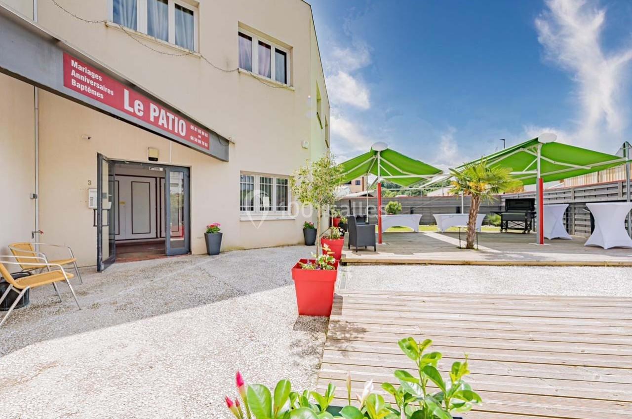 Entrée d'un bâtiment avec terrasse aménagée, parasols verts, plantes en pots et mobilier extérieur.