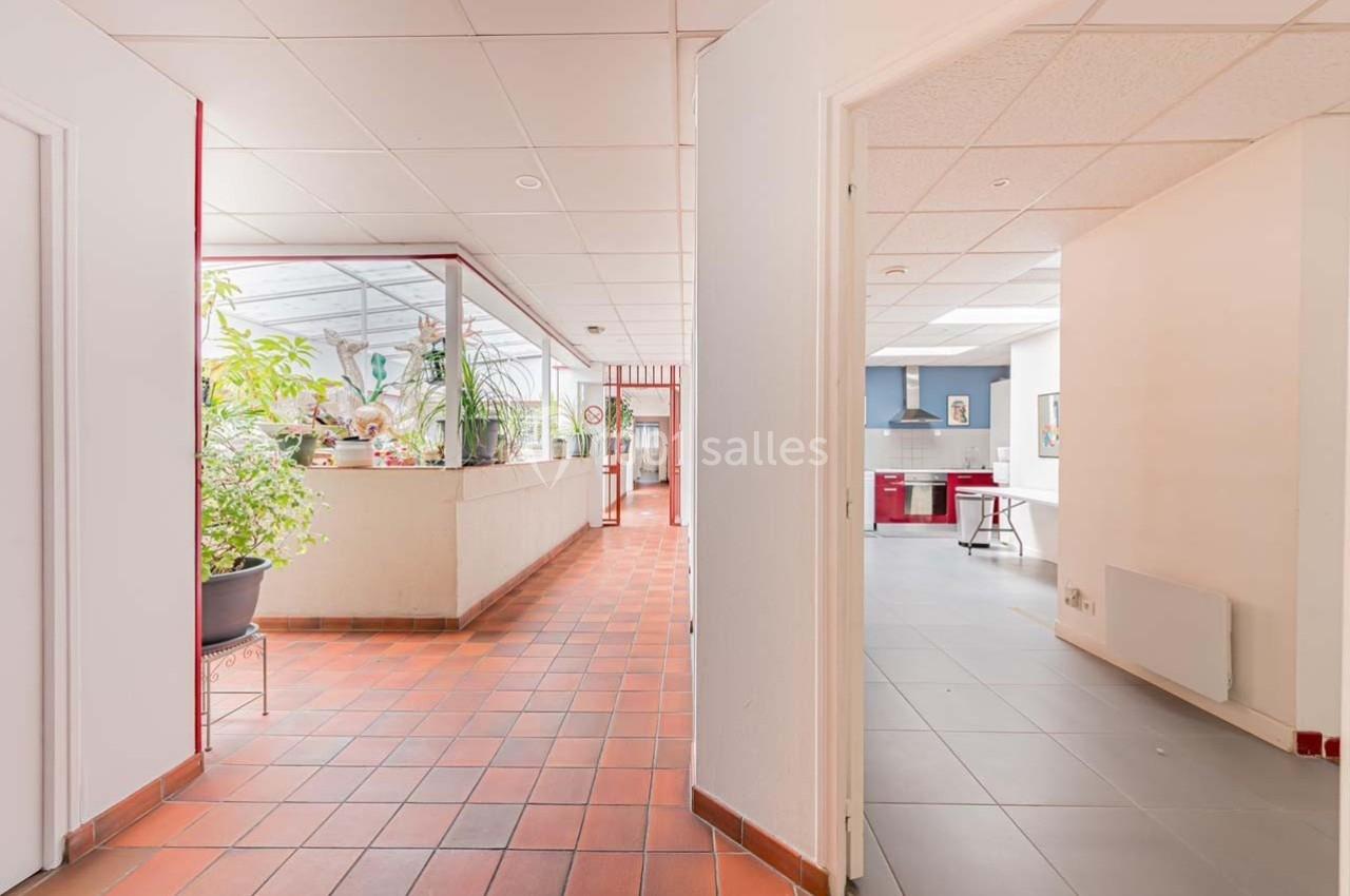 Vue intérieure d'un espace lumineux avec un sol en carrelage, une cuisine moderne et une véranda avec des plantes.