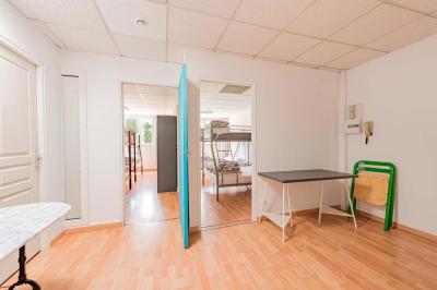 Chambre lumineuse avec lit double, tables de chevet, lampes, sol en bois clair et fenêtres donnant sur l'extérieur.