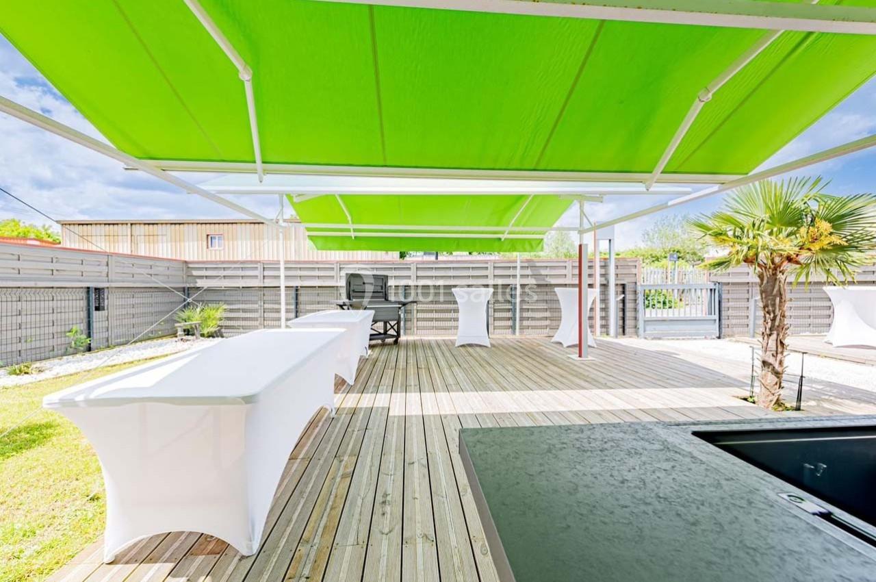 Terrasse en bois avec des tables habillées de nappes blanches, abritée par des toiles tendues vertes.
