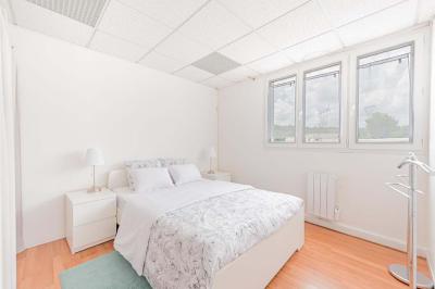 Chambre lumineuse avec lit double, tables de chevet, lampes, sol en bois clair et fenêtres donnant sur l'extérieur.