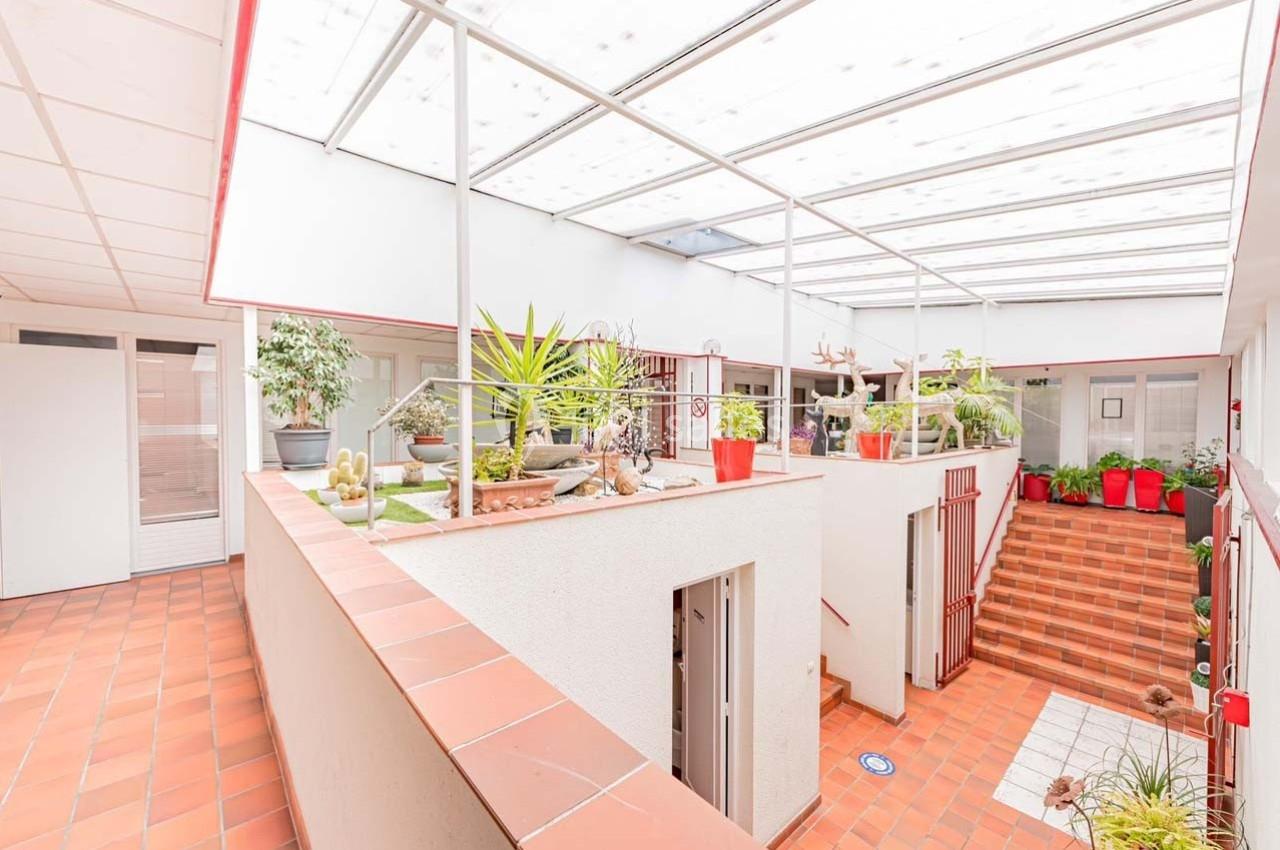 Cour intérieure lumineuse avec toit en verre, plantes en pots et escaliers en carrelage rouge.