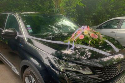 SUV noir décoré d'un bouquet de fleurs sur le capot, stationné sur un parking entouré de végétation.