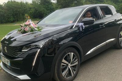 SUV noir décoré d'un bouquet de fleurs sur le capot, stationné sur un parking entouré de végétation.