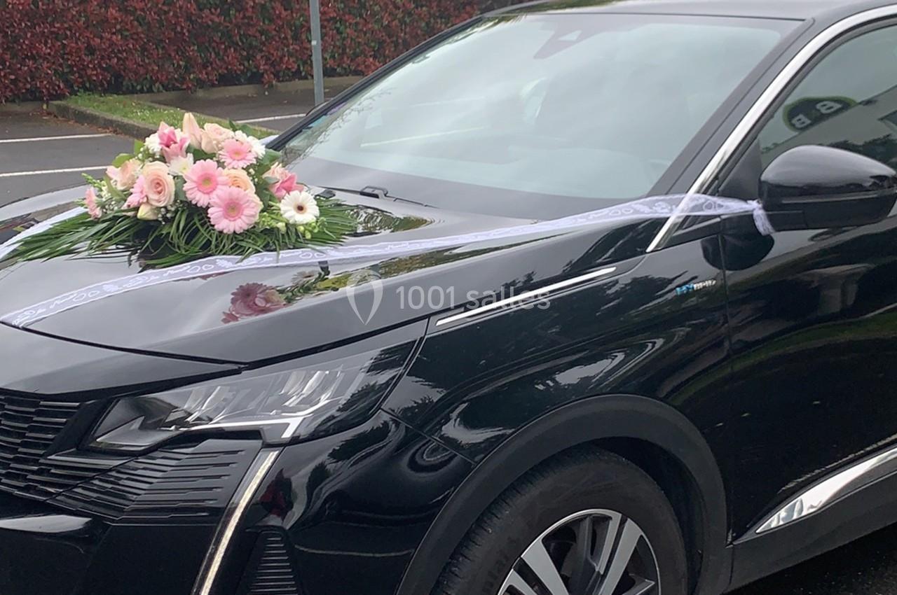 Voiture noire décorée d'un bouquet de fleurs roses et blanches sur le capot, avec rubans blancs.