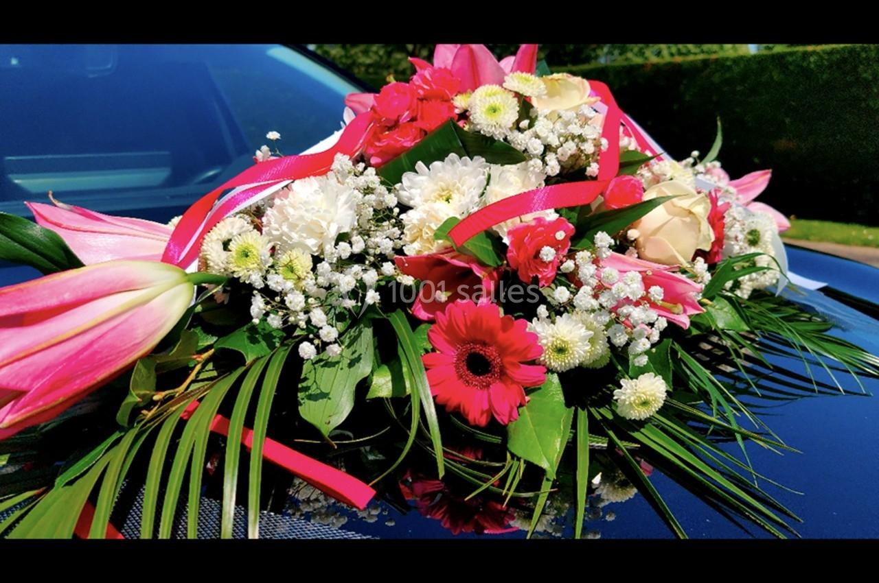 Composition florale colorée avec des lys, roses, gerberas et feuillages, posée sur le capot d'une voiture.
