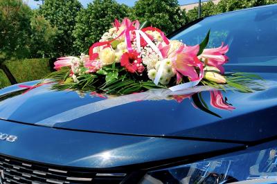 SUV noir décoré d'un bouquet de fleurs sur le capot, stationné sur un parking entouré de végétation.