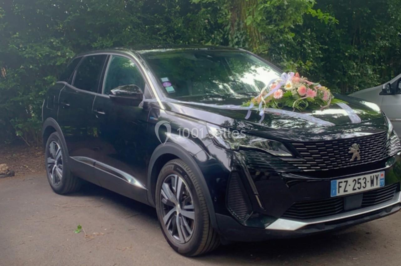 SUV noir décoré d'un bouquet de fleurs sur le capot, stationné sur un parking entouré de végétation.
