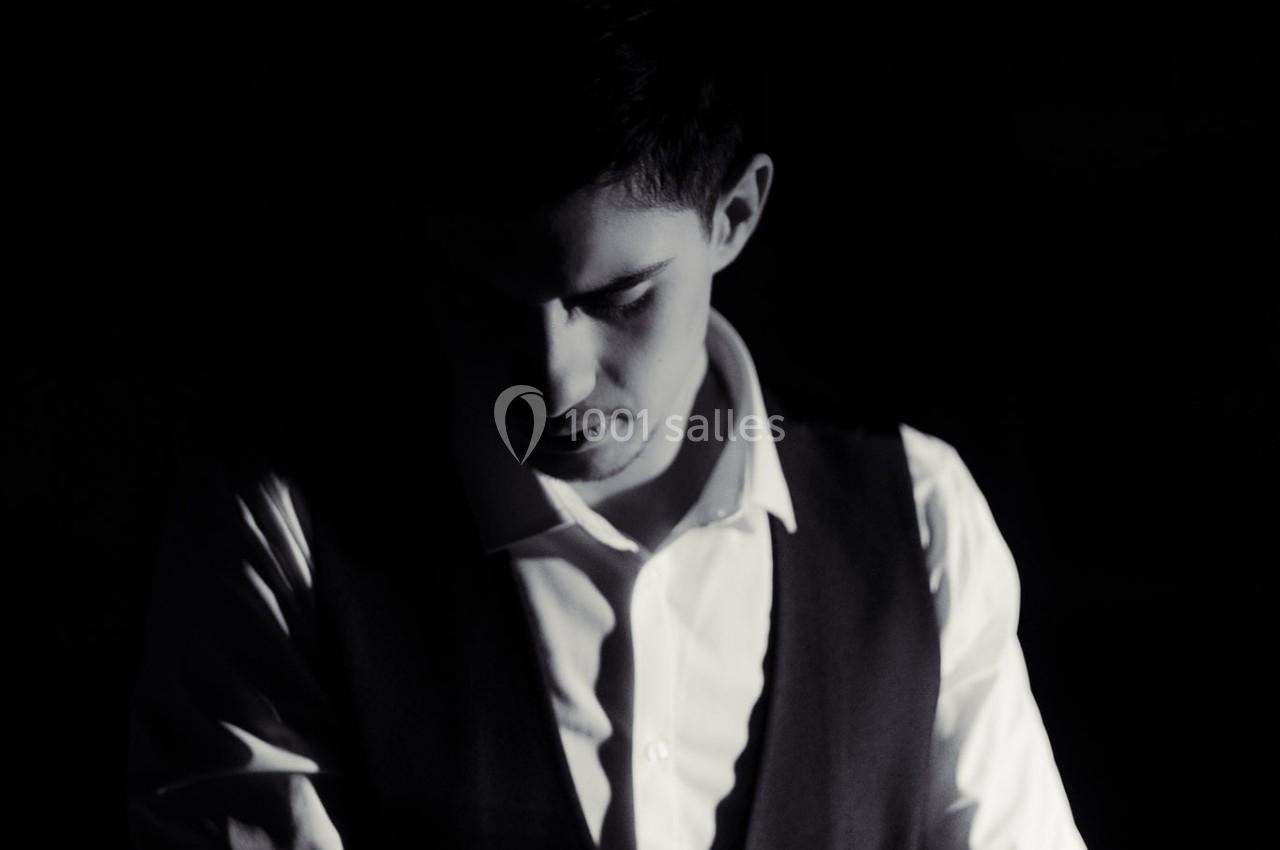 Homme en chemise blanche et gilet sombre, partiellement éclairé dans une ambiance sombre.