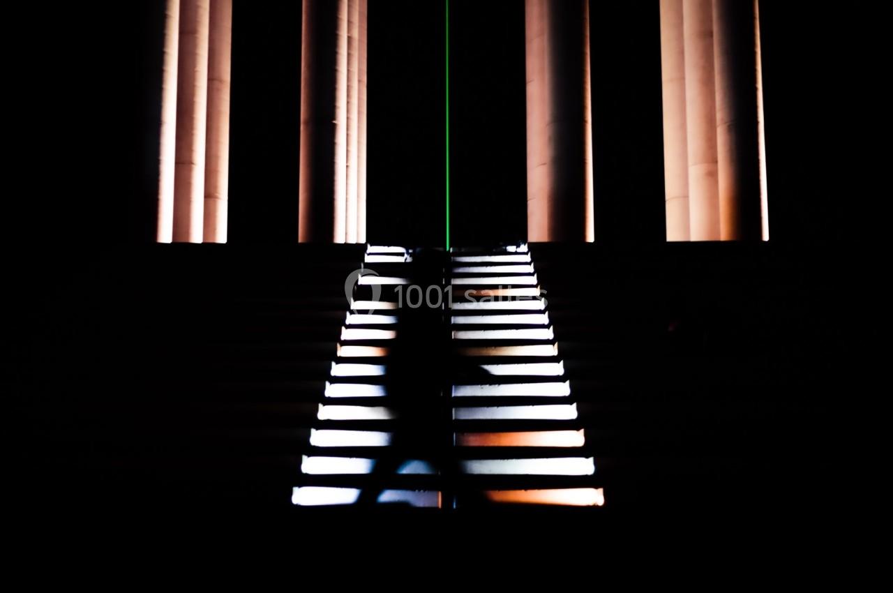 Silhouette floue d'une personne montant un escalier éclairé, avec des colonnes lumineuses en arrière-plan.