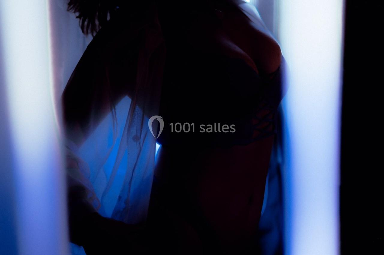 Silhouette d'une personne en lingerie et chemise légère, éclairée par une lumière bleutée près d'une fenêtre.