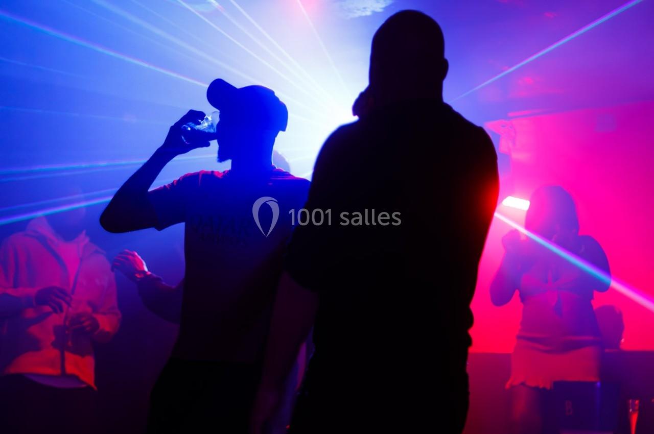 Personnes dansant et discutant dans une ambiance de boîte de nuit avec des lumières colorées et des lasers.