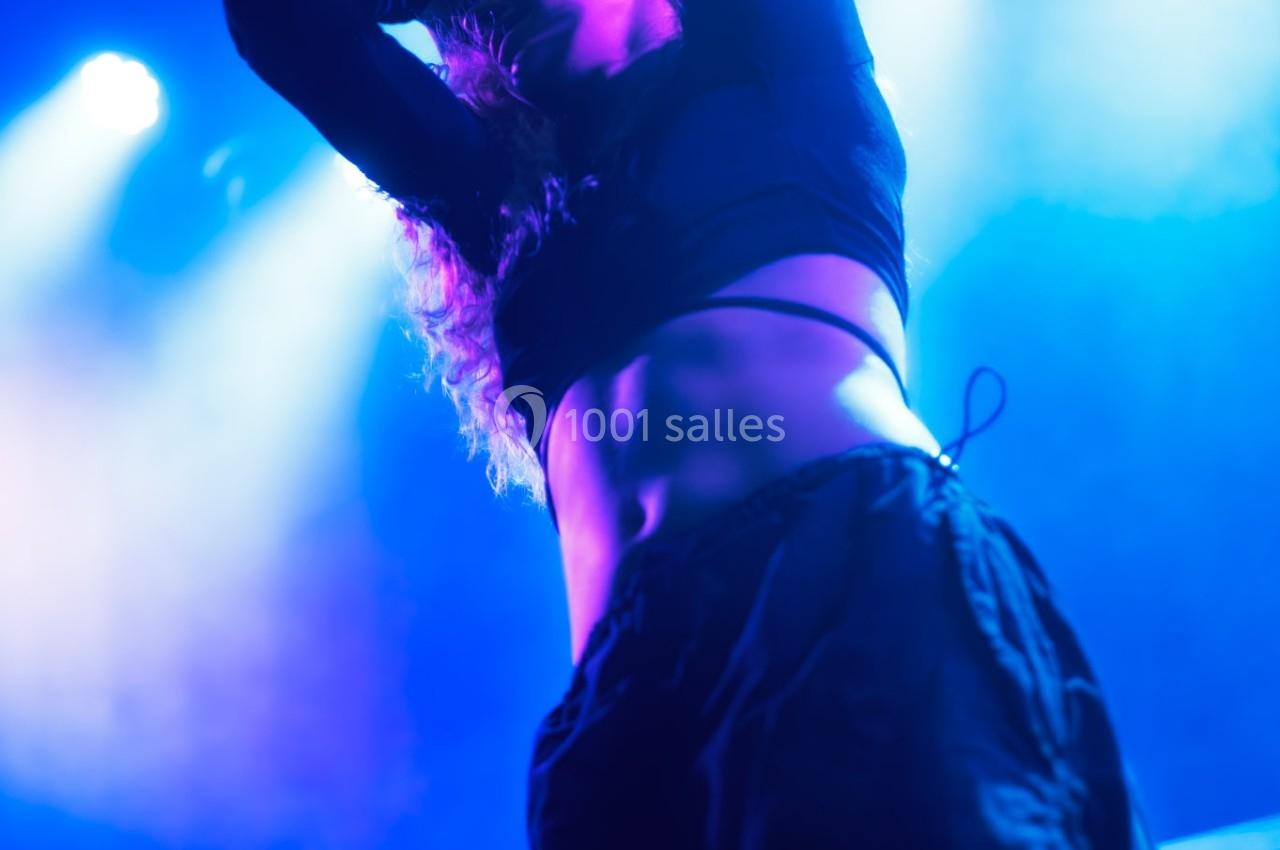 Personne dansant sur scène sous des lumières bleues et violettes, ambiance de concert dynamique.