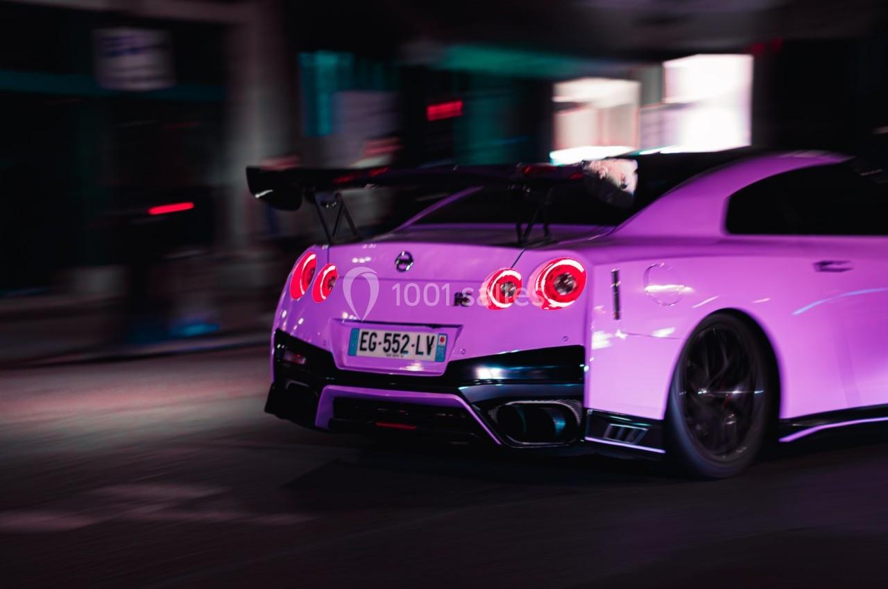 Voiture sportive blanche roulant rapidement dans une rue éclairée par des néons, vue de trois quarts arrière.