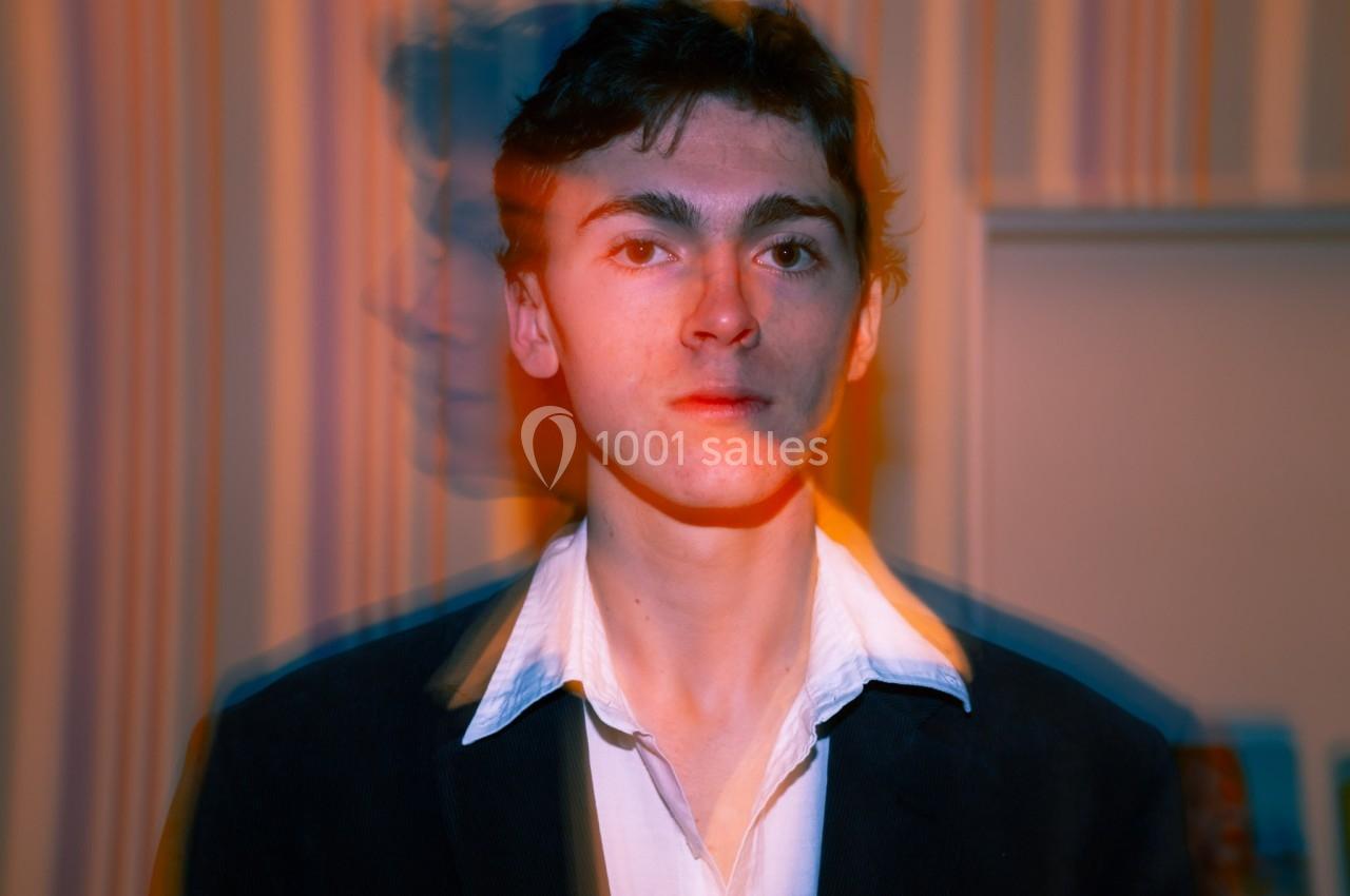 Un homme en chemise blanche et veste sombre, photographié avec un effet de flou et de dédoublement coloré.