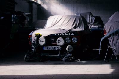 Voiture sportive bleue stationnée sur une place pavée devant un monument en bronze et des bâtiments historiques.