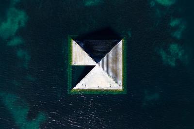 Voiture sportive bleue stationnée sur une place pavée devant un monument en bronze et des bâtiments historiques.