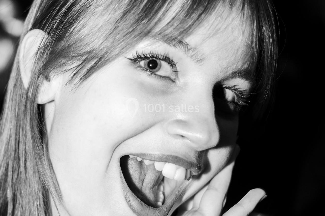 Femme souriante en gros plan, exprimant la joie avec une main posée sur son visage, éclairage en noir et blanc.