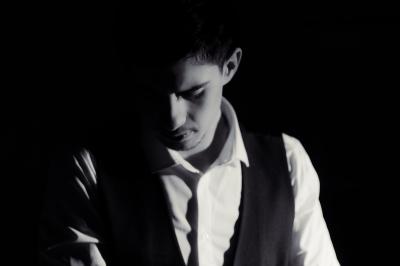 Femme assise sur un banc en extérieur, portant un sweat noir, avec un ciel bleu et des bâtiments en arrière-plan.