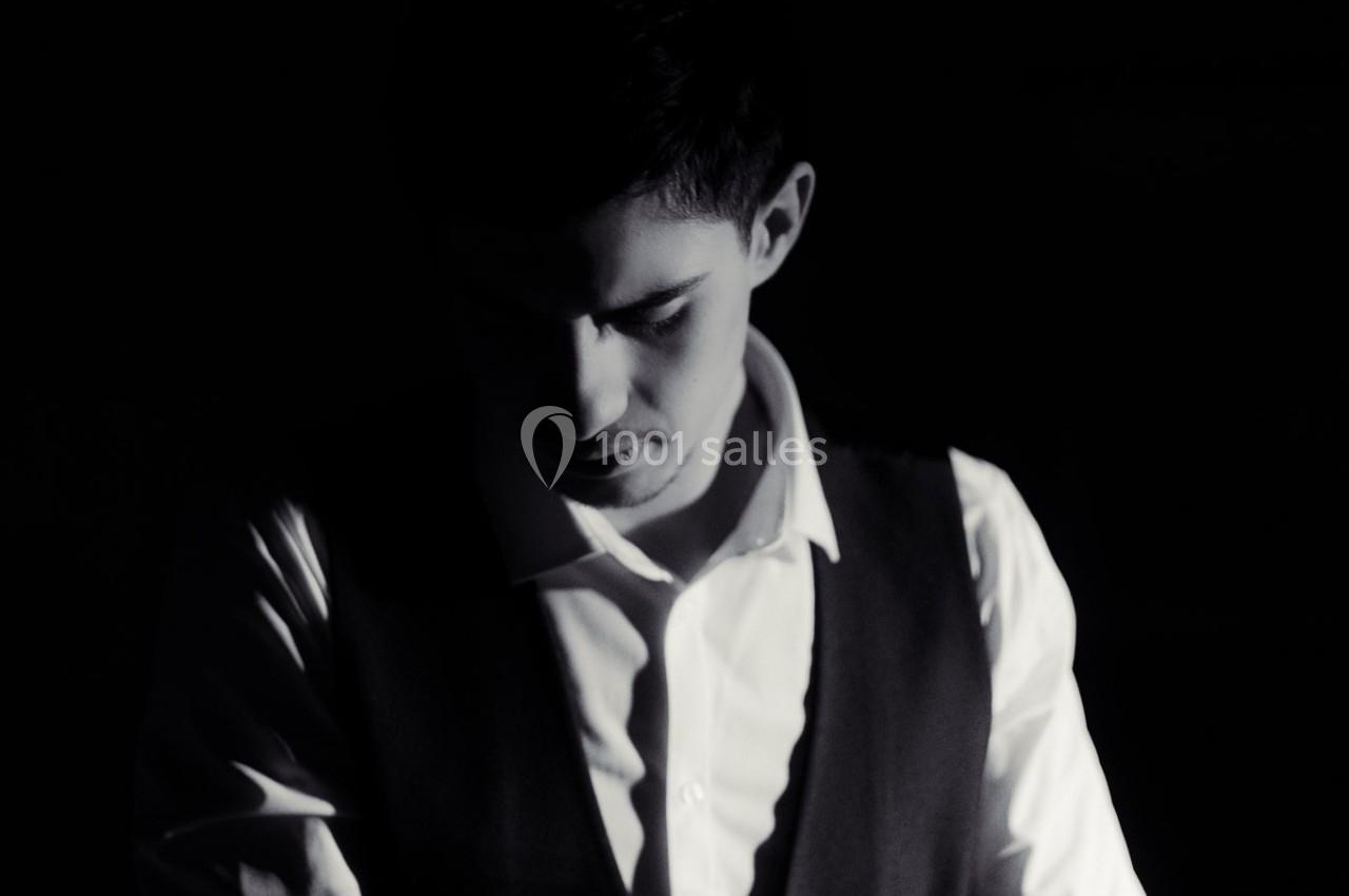 Homme en chemise blanche et gilet sombre, partiellement éclairé dans une ambiance sombre.