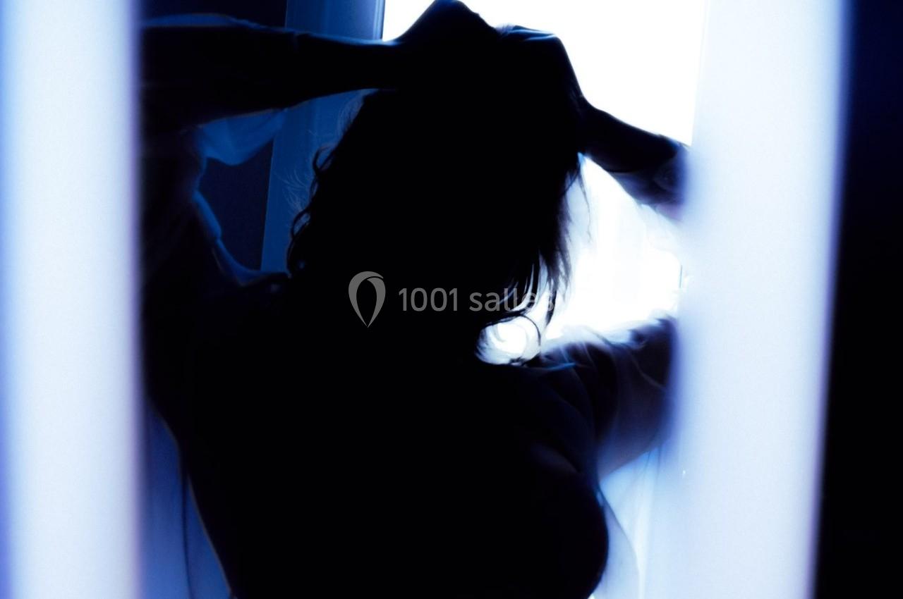 Silhouette d'une personne de dos, les mains dans les cheveux, éclairée par une lumière vive en arrière-plan.