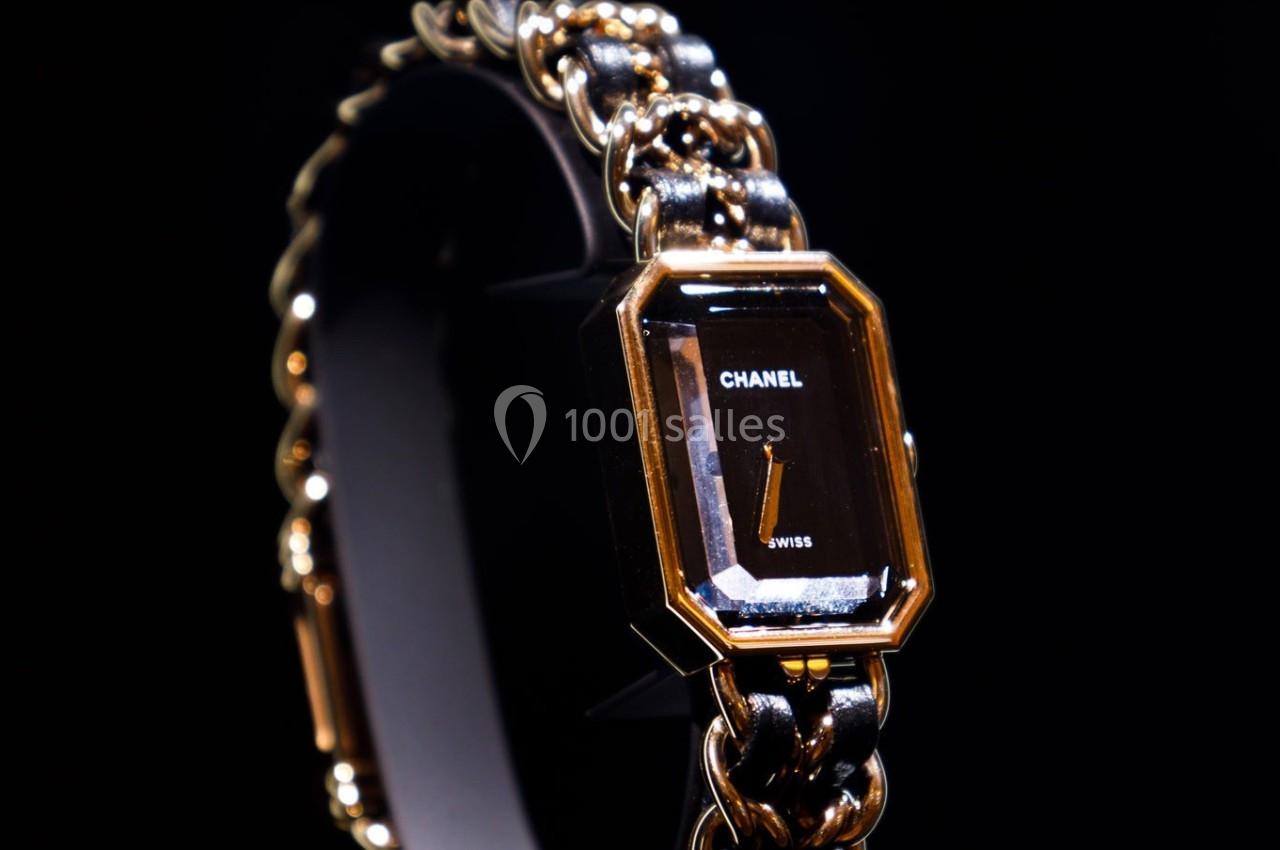 Montre élégante avec cadran noir rectangulaire, boîtier doré et bracelet en chaîne métallique entrelacée.