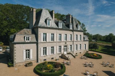 Un couple de mariés marche vers un château en pierre avec des volets blancs, entouré de quelques invités.