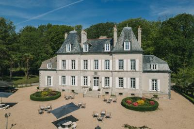 Un couple de mariés marche vers un château en pierre avec des volets blancs, entouré de quelques invités.