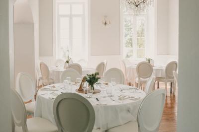 Un couple de mariés marche vers un château en pierre avec des volets blancs, entouré de quelques invités.