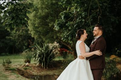Un couple de mariés marche vers un château en pierre avec des volets blancs, entouré de quelques invités.