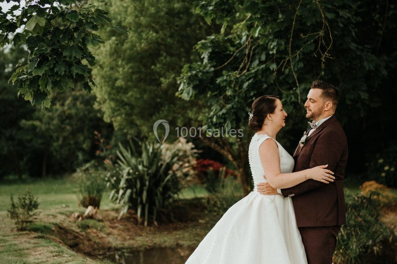 Un couple en tenue de mariage se tient près d'un petit étang dans un jardin verdoyant.