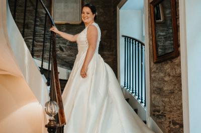 Un couple de mariés marche vers un château en pierre avec des volets blancs, entouré de quelques invités.