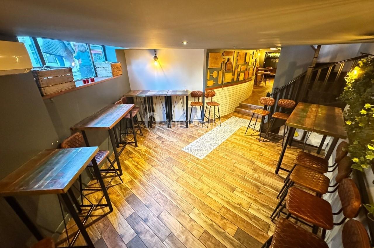Salle lumineuse avec parquet en bois, tables hautes, tabourets en cuir et décoration murale chaleureuse.
