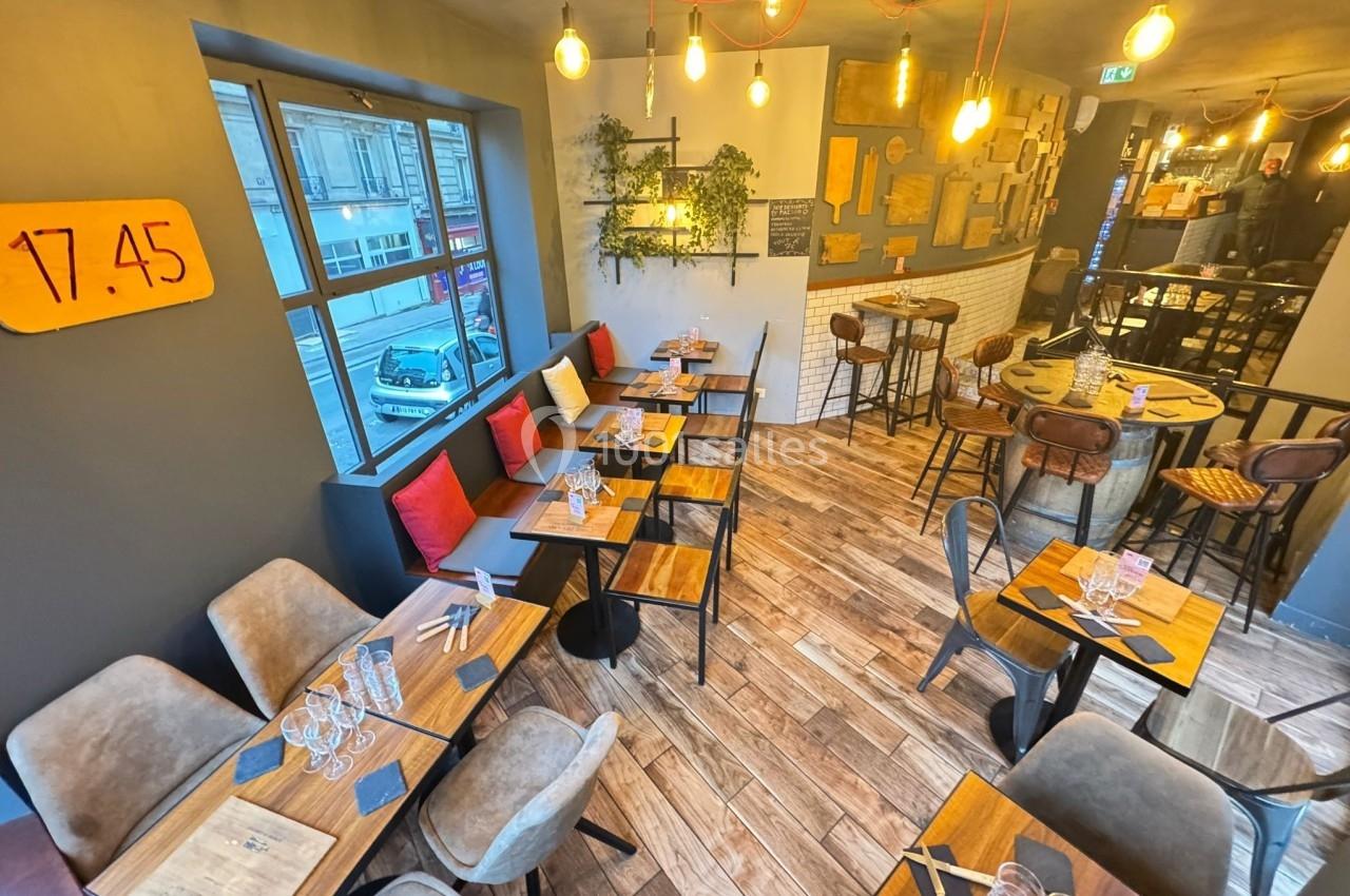 Salle de restaurant lumineuse avec tables en bois, chaises rembourrées, décorations murales et grandes fenêtres donnant sur…