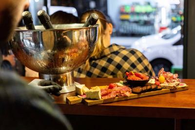 Des mains trinquent avec des verres au-dessus d'une table garnie de charcuterie, fromages et pains.