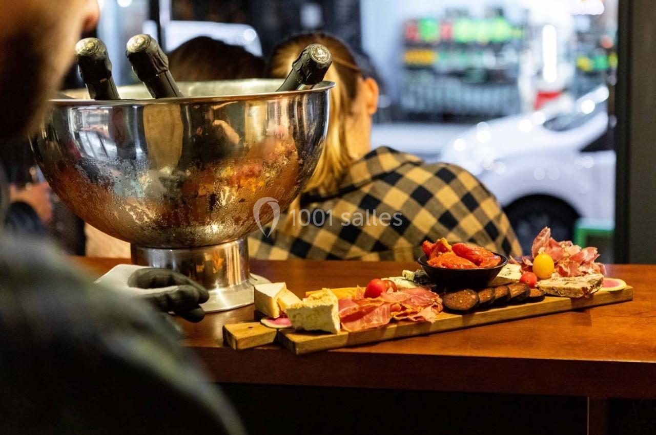 Plateau de charcuterie et fromages avec pain et légumes, posé sur un comptoir en bois près d'un seau à champagne.