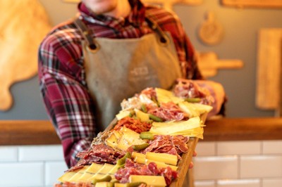 Des mains trinquent avec des verres au-dessus d'une table garnie de charcuterie, fromages et pains.