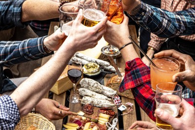 Des mains trinquent avec des verres au-dessus d'une table garnie de charcuterie, fromages et pains.