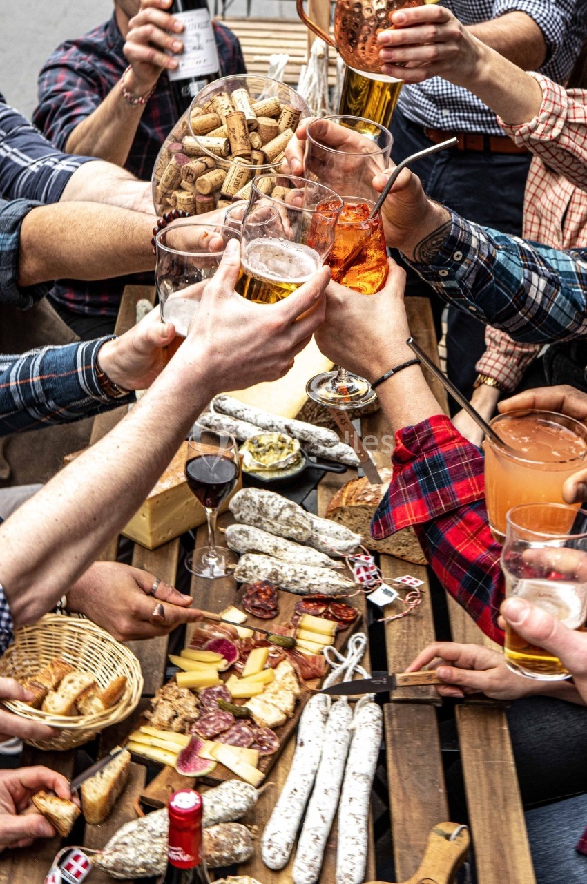 Des mains trinquent avec des verres au-dessus d'une table garnie de charcuterie, fromages et pains.