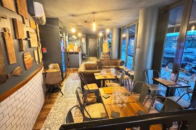 Salle de restaurant chaleureuse avec mobilier en bois, grandes fenêtres et éclairage suspendu.