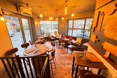 Salle de restaurant chaleureuse avec mobilier en bois, grandes fenêtres et éclairage suspendu.