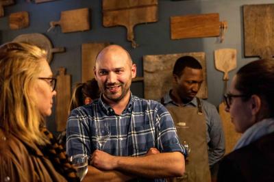 Salle de restaurant chaleureuse avec mobilier en bois, grandes fenêtres et éclairage suspendu.