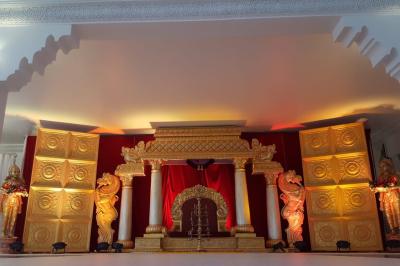 Décor de scène avec colonnes blanches, ornements dorés, rideau rouge et statues sculptées sur les côtés.