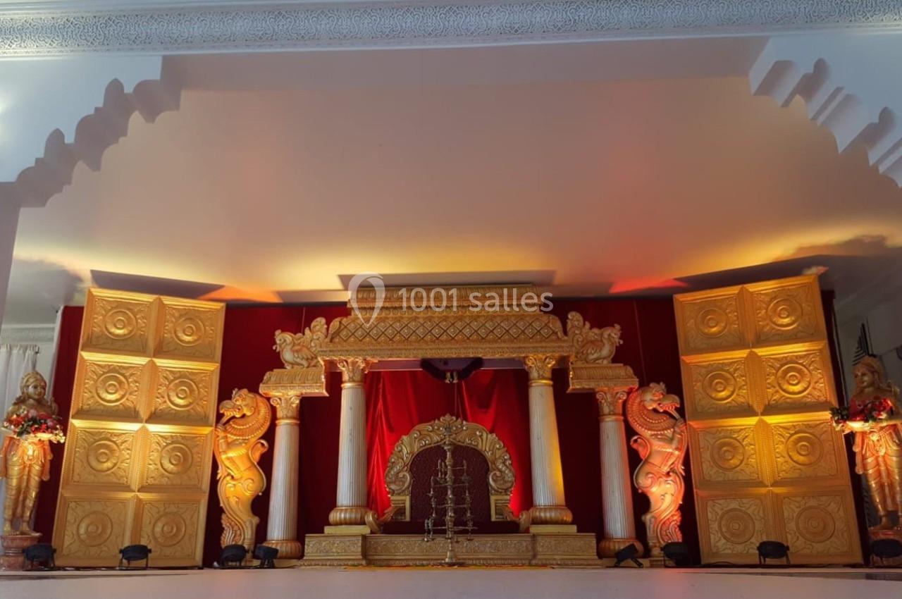 Décor de scène avec colonnes blanches, ornements dorés, rideau rouge et statues sculptées sur les côtés.