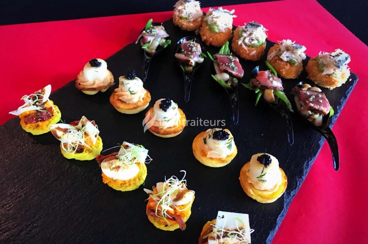 Plateau d'amuse-bouches variés disposés sur une ardoise noire, comprenant bouchées salées et cuillères garnies.