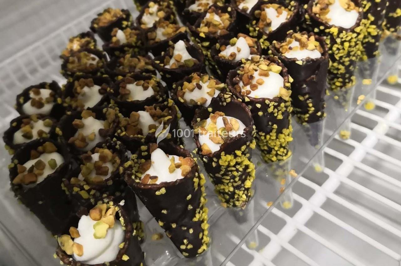 Cônes en chocolat garnis de crème et décorés de morceaux de pistache, disposés sur un plateau transparent.