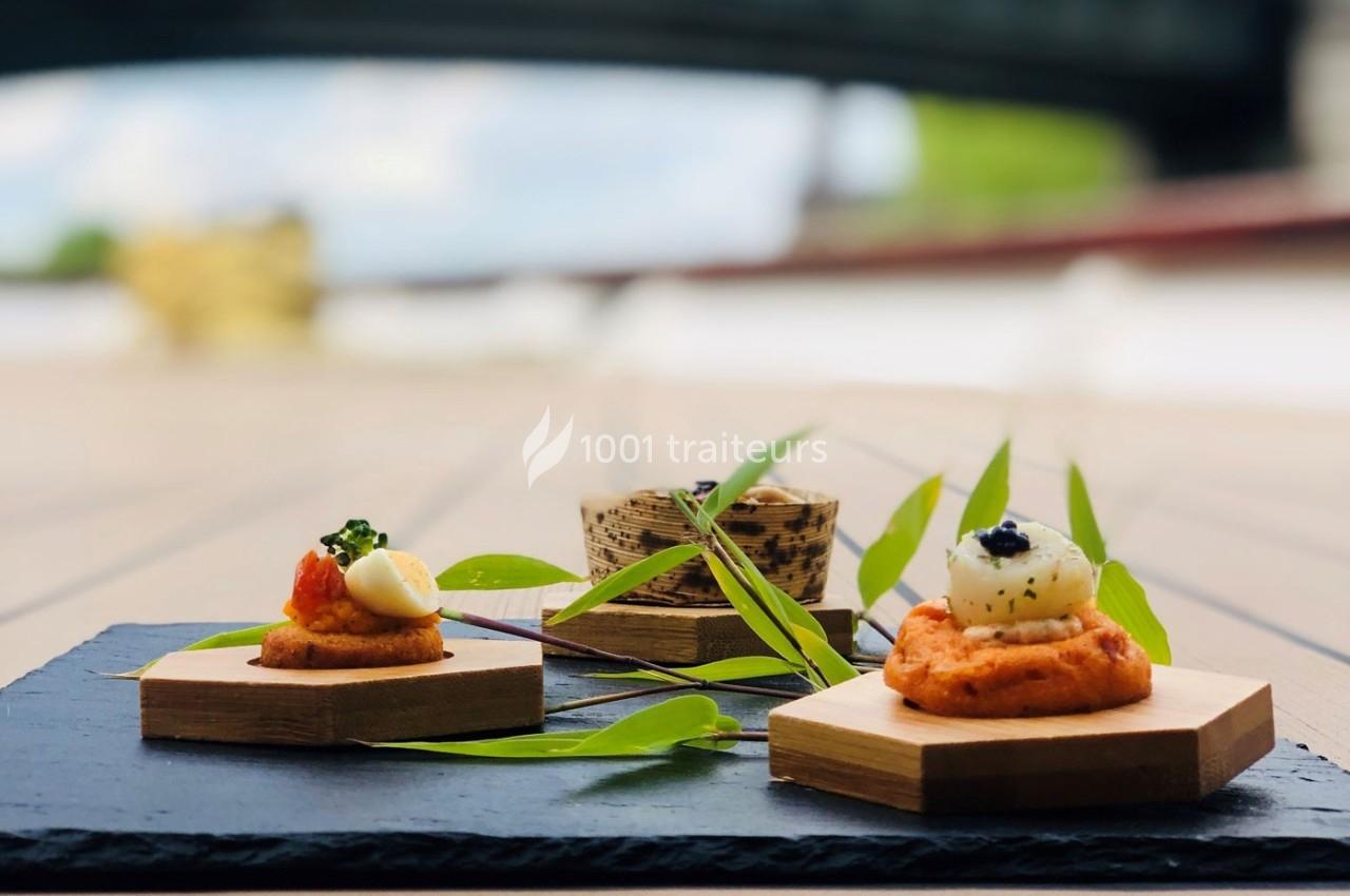 Assortiment de bouchées gastronomiques présentées sur des supports en bois, décorées de feuilles vertes.