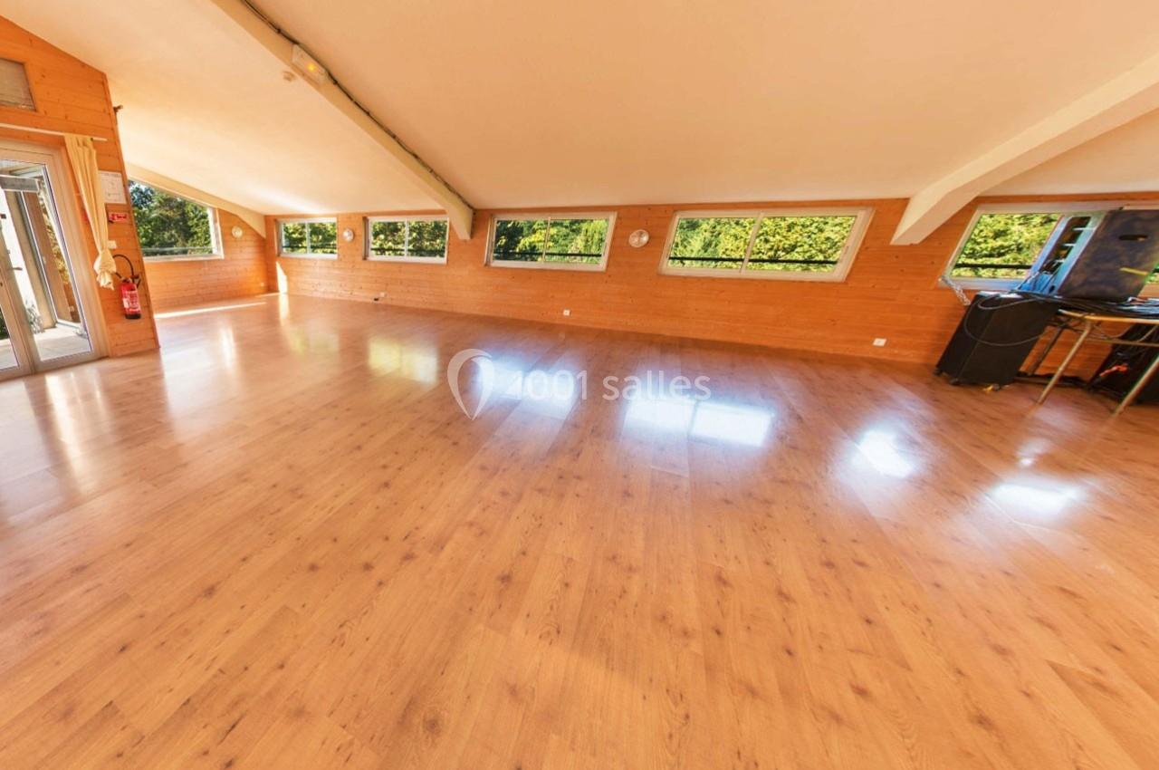 Salle spacieuse avec parquet en bois clair, murs en bois et grandes fenêtres offrant une vue sur la végétation extérieure.