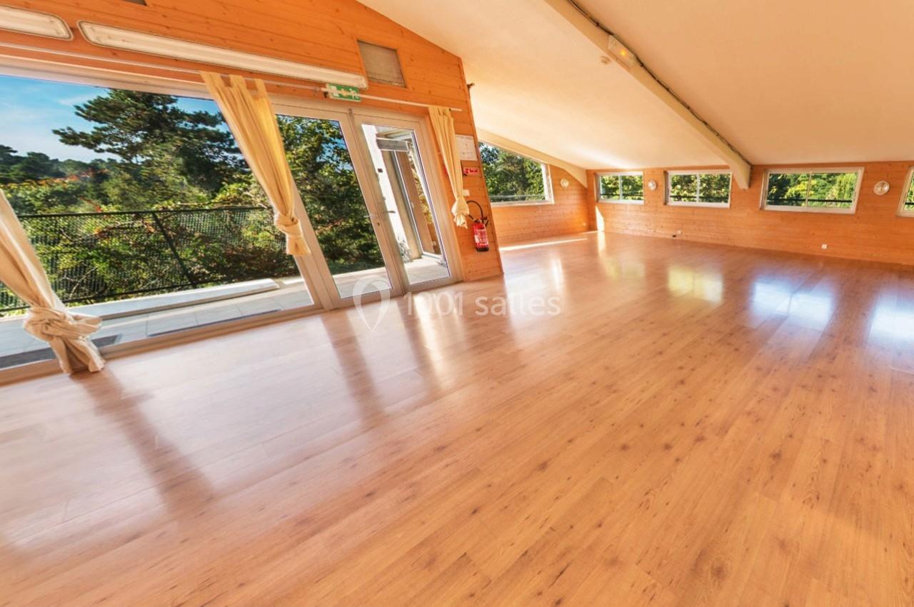 Salle lumineuse avec parquet en bois, grandes fenêtres et vue sur un espace extérieur arboré.